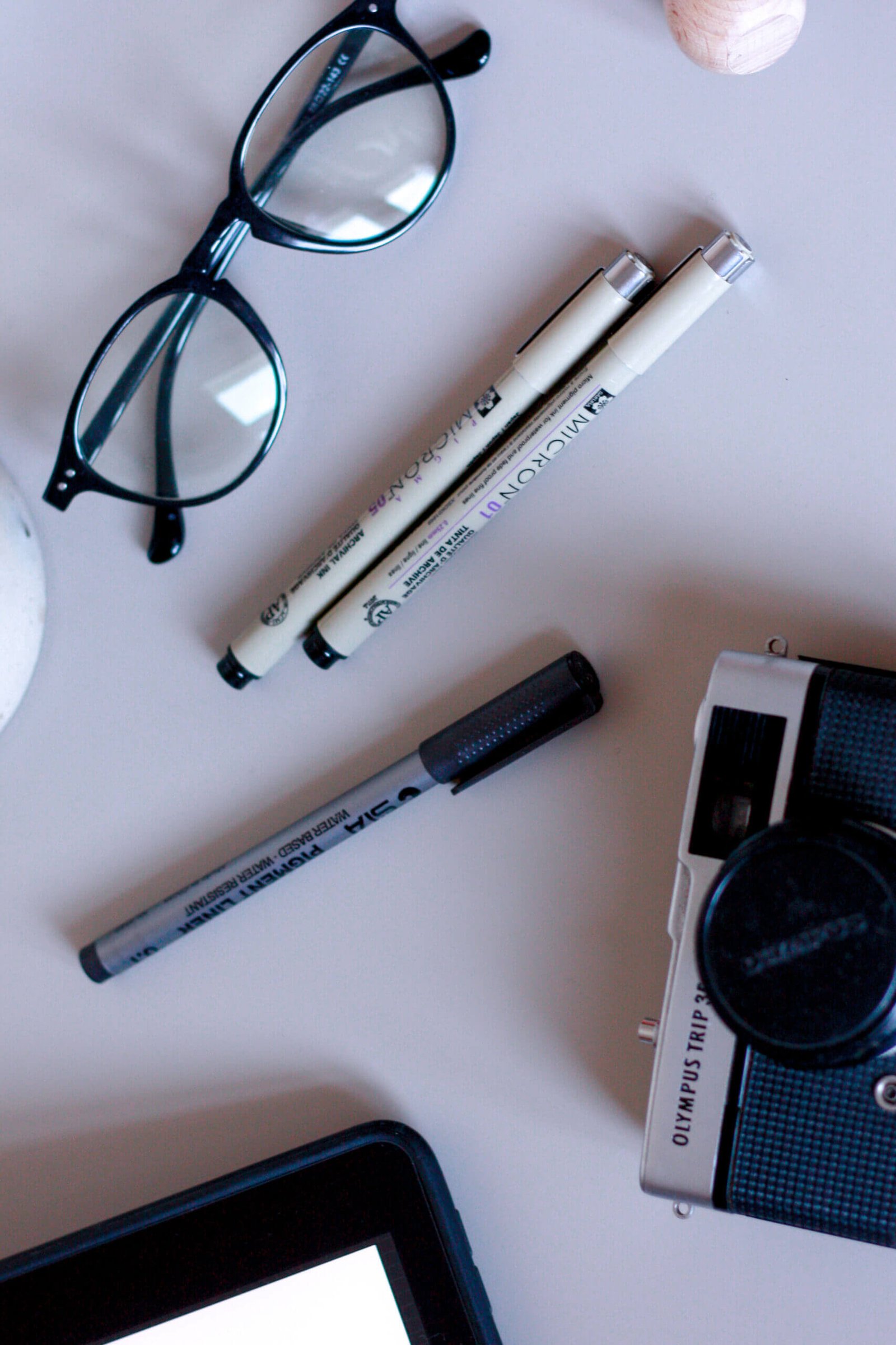 A flatlay of some desk items, including pens, glasses, a camera and an iPad displaying a website